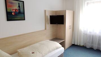 Ein Hotelzimmer mit einem Bett, einem an einem Holzkasten montierten Fernseher und einem Gemälde an der Wand.
