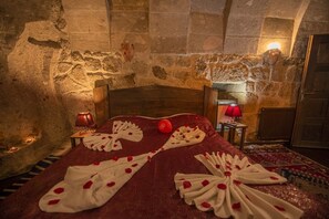 A stone-walled room with a bed, a red blanket, and rose petals arranged on the bed. - Karamanli Konagi (Guzelyurt)