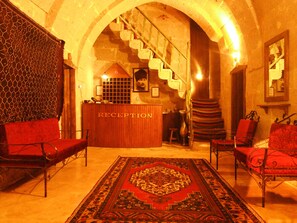 A reception area with a wooden reception desk, red upholstered chairs, a patterned rug, and a staircase leading to an upper level. - Karamanli Konagi (Guzelyurt)