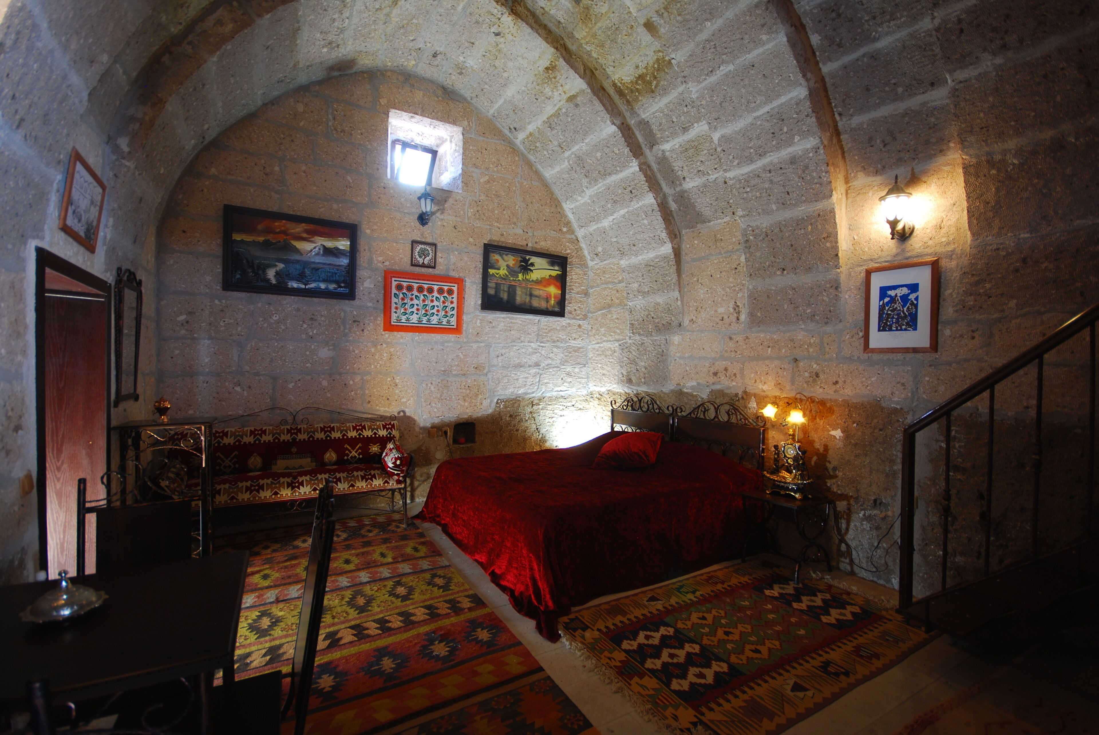 Una habitación con una cama, una mesa y una silla. Hay cuadros en la pared y una ventana.