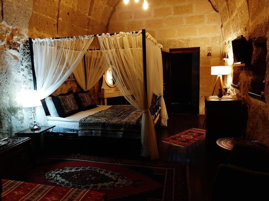 A dimly lit room with a four-poster bed, a small table, and a lamp.