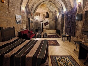 A cozy, rustic room with a stone wall, a bed with patterned bedding, a red sofa, and a small table with a lamp. - Karamanli Konagi (Guzelyurt)