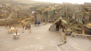 Una terraza con mesas y sillas de piedra, un banco azul pequeño y una estructura rústica de piedra.