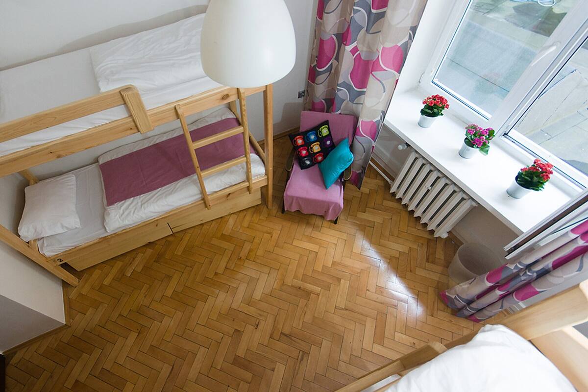 A bunk bed with a wooden frame, a small table with a pink tablecloth, and a window with curtains.