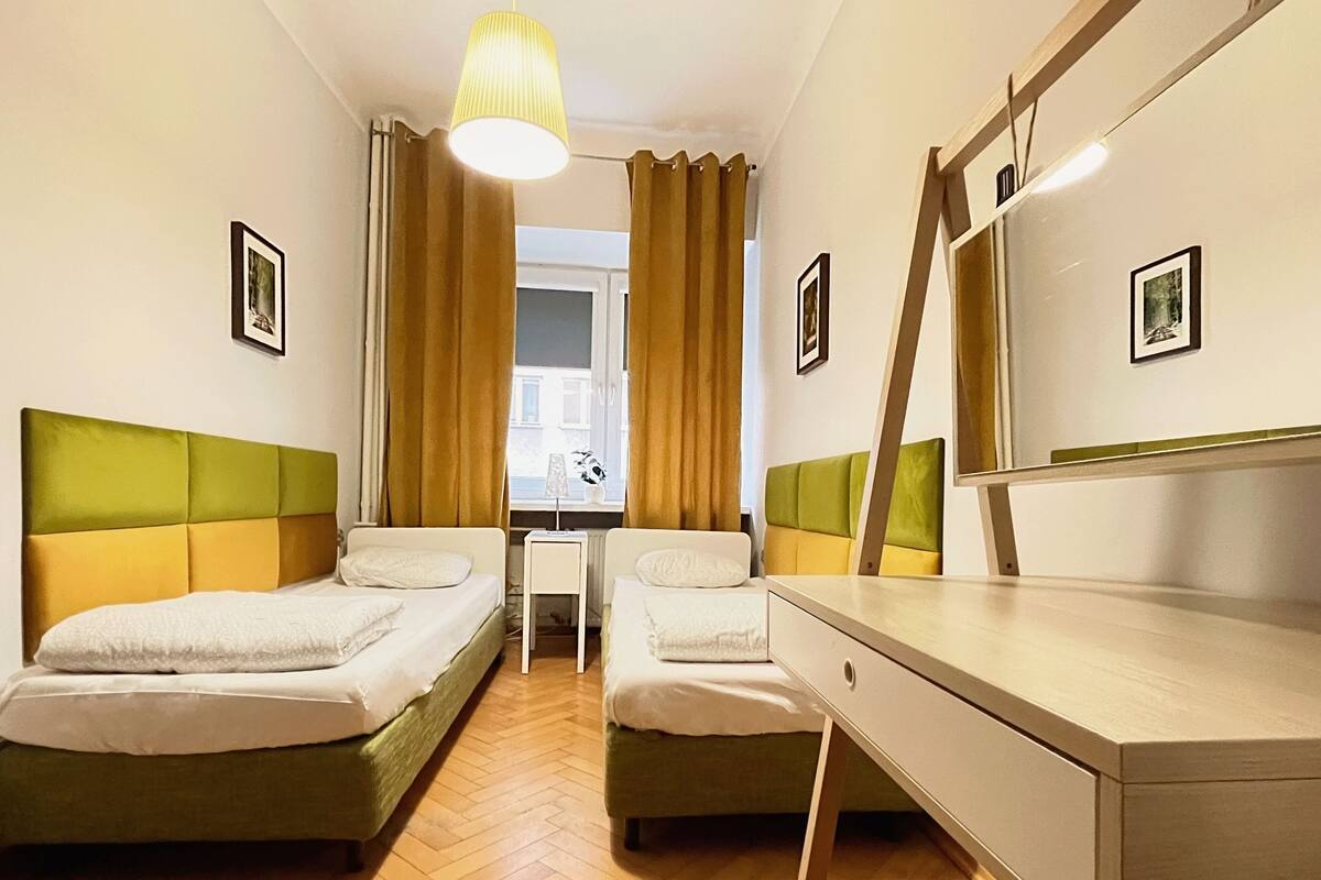 A hotel room with two beds, a desk, a chair, a mirror, and a window with curtains.