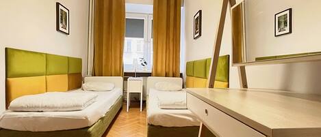 A hotel room with two beds, a desk, a chair, a mirror, and a window with curtains.