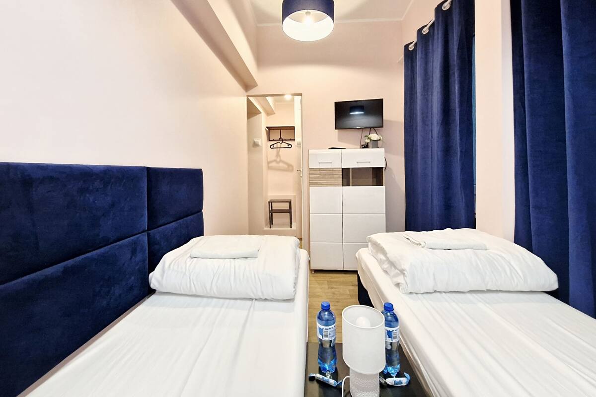 A hotel room with two beds, a TV, a wardrobe, and a shower area.