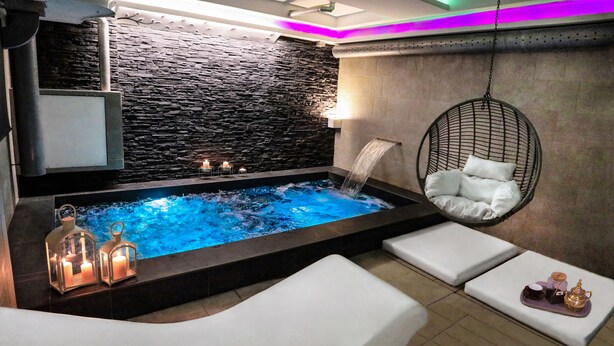 Un área de spa con pared de piedra, bañera de hidromasaje, velas y una silla colgante.