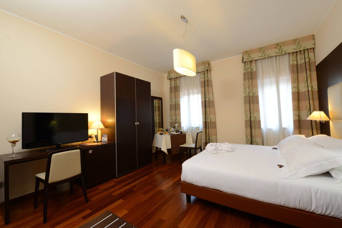 A hotel room with a bed, a desk, a TV, and a wardrobe.