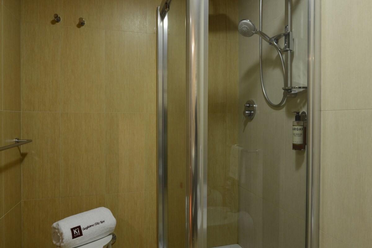A glass-enclosed shower area with a white stool and a bottle of hand soap.