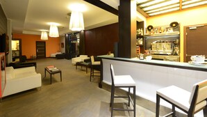 Un moderno vestíbulo de hotel con una zona de bar, asientos y una cocina visible al fondo.