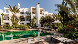 A pool area with lounge chairs and a building with balconies.