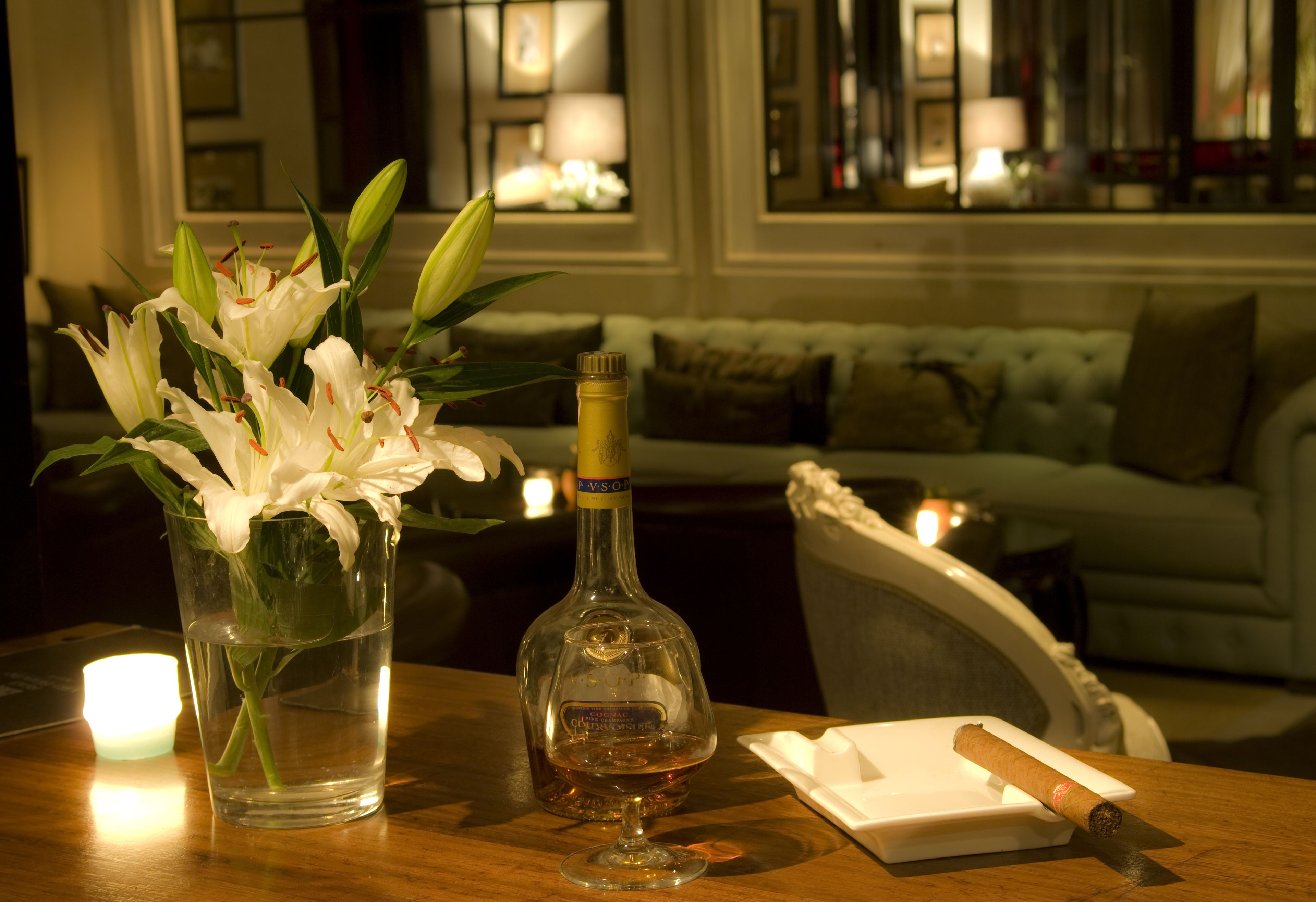 Una mesa con un jarrón de flores blancas, una botella de licor y un puro.