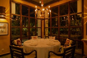 A dining room with a round table set for four, surrounded by chairs, large windows, and a chandelier.
