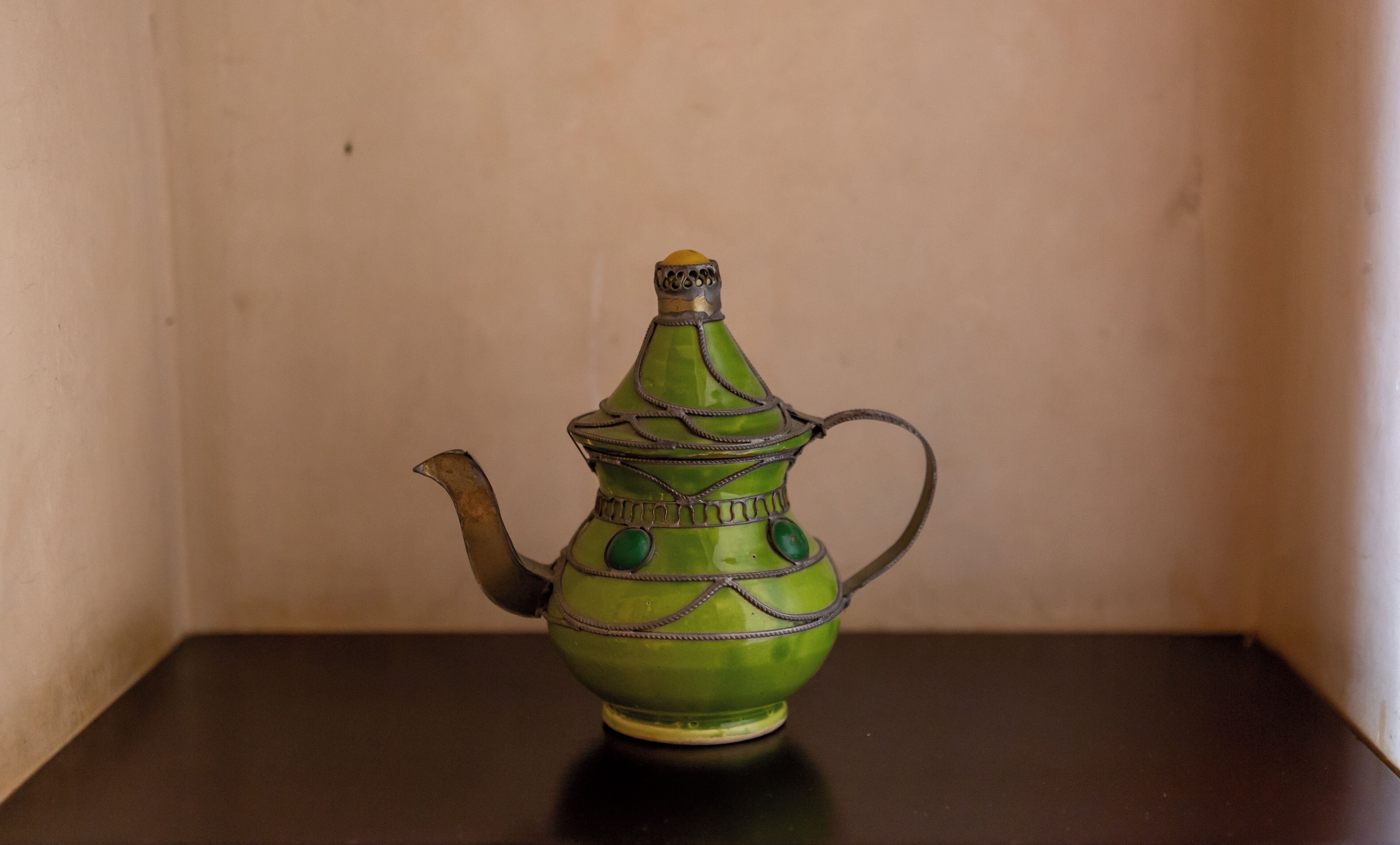 A green ceramic teapot with a spout and handle on a dark surface.