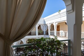 A balcony with white curtains, a wrought iron railing, and a view of a building with arches and a balcony.