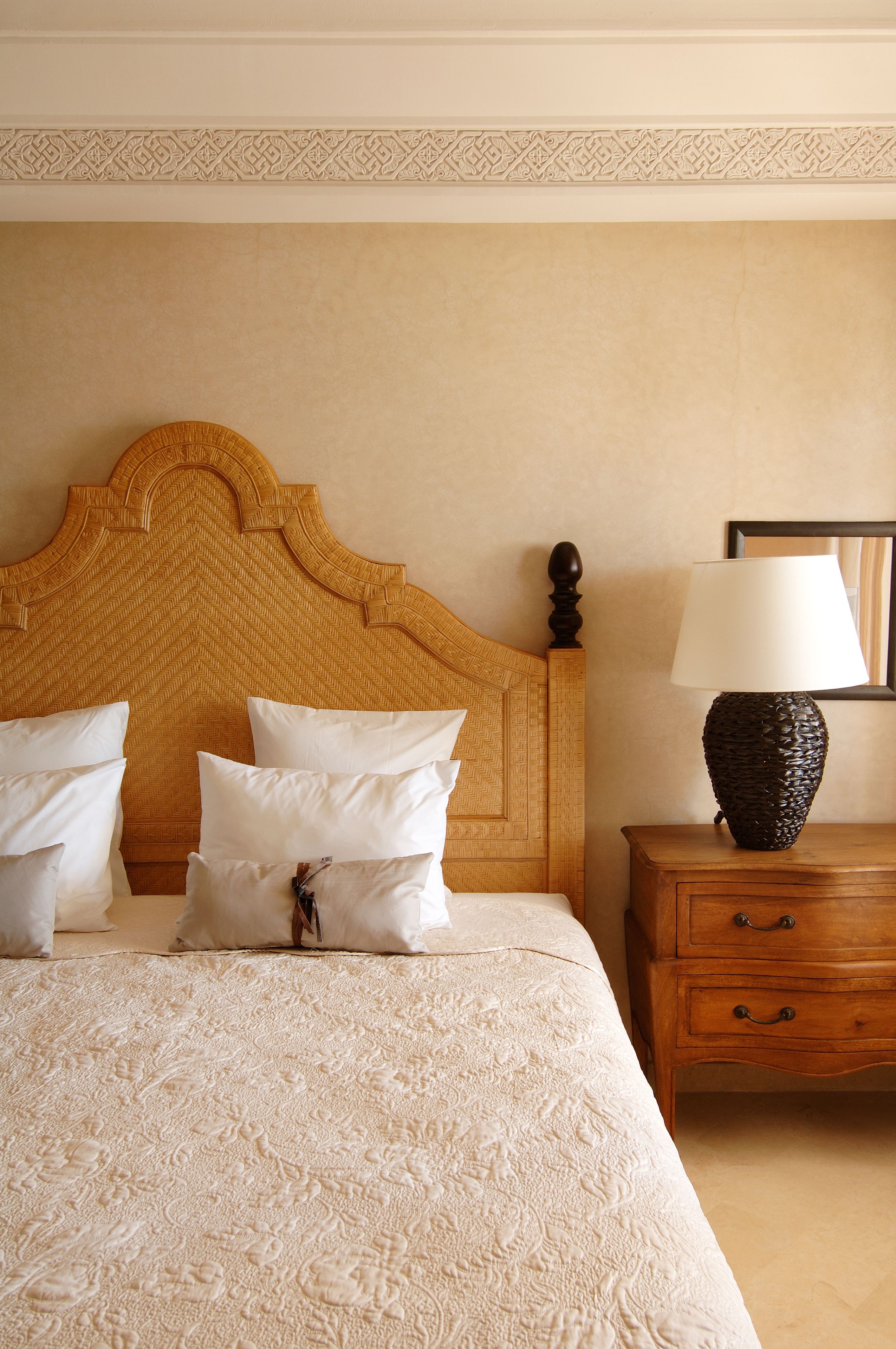 Een net opgemaakt bed met een gebreid sprei, een houten hoofdbord en een nachtkastje met een lamp en een ingelijste foto.