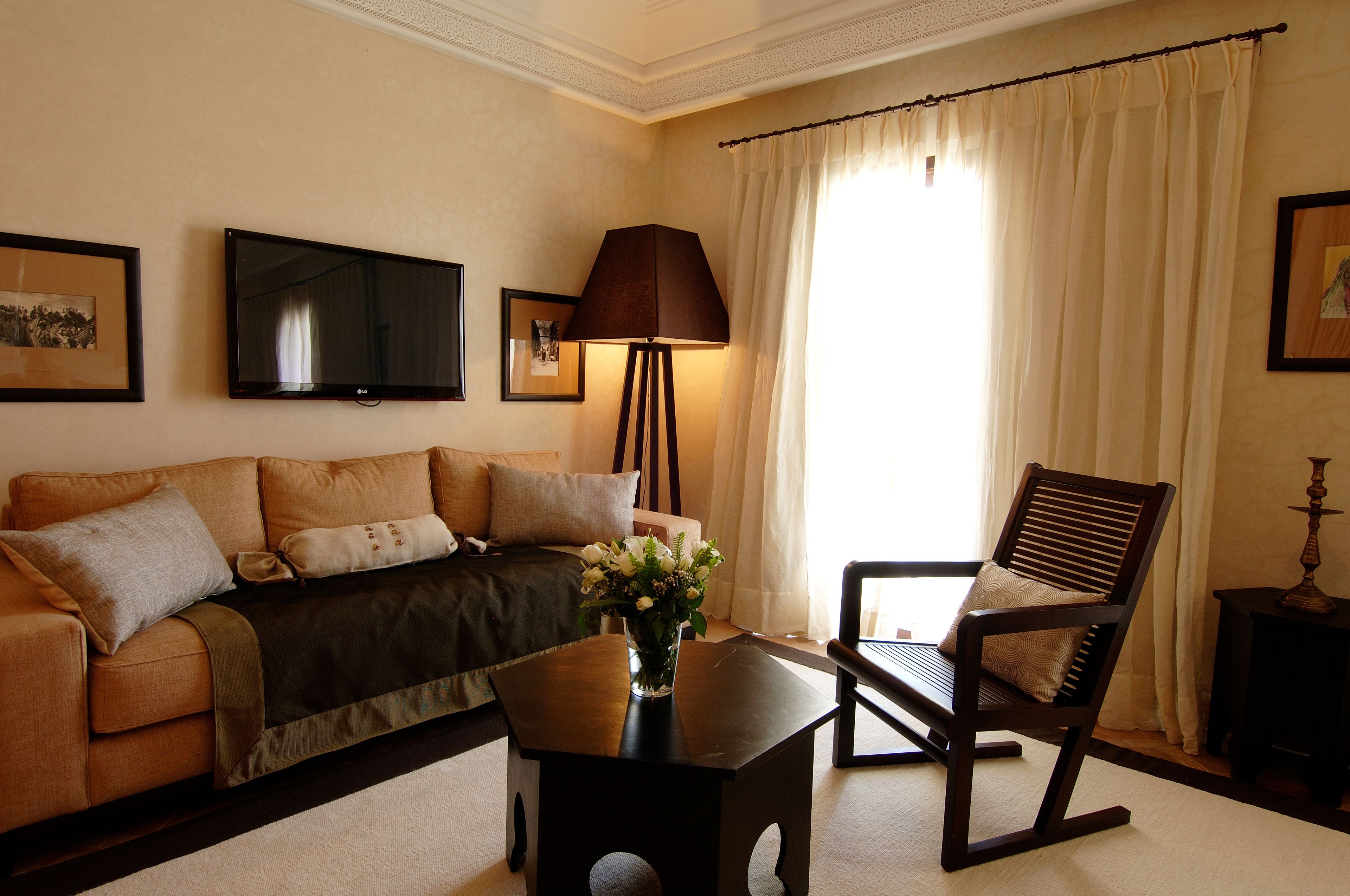 A living room with a sofa, a coffee table with a vase, a lamp, a chair, and a television on the wall.