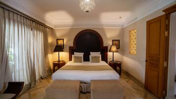 A hotel room with a large bed, two bedside tables with lamps, a wooden door, and a large window with curtains.