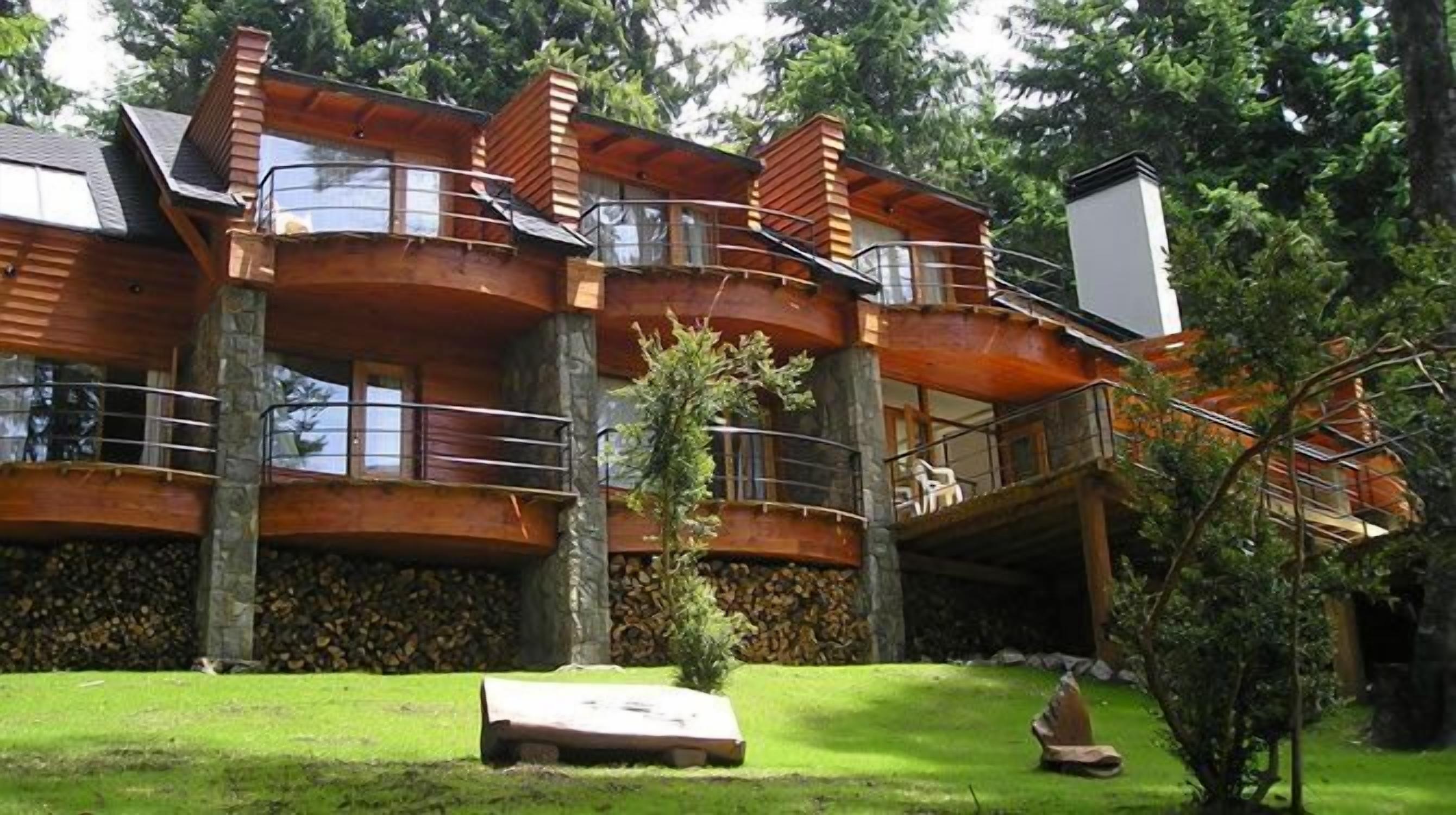 Una cabaña de troncos con varios balcones, base de piedra y un césped bien cuidado.