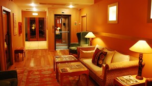 Un hall de hotel con piso de madera, un sofá, una silla, una mesa con revistas y una lámpara.