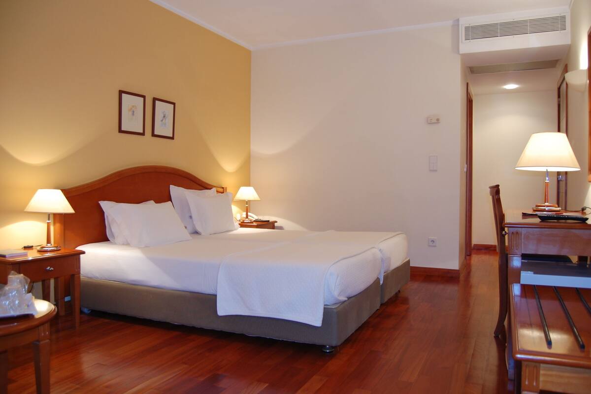 Une chambre d’hôtel comprenant un lit, deux tables de chevet avec des lampes, une chaise en bois et un bureau avec une lampe.
