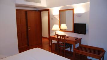 A hotel room with a bed, a desk with two lamps, a chair, a television, and a wardrobe.