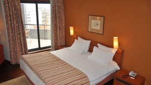 Habitación de hotel con una cama grande, dos lámparas de noche, una mesita de noche con un teléfono y vistas a la ciudad a través de la ventana.