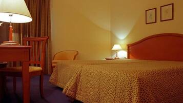 Quarto de hotel com uma cama, duas cadeiras, uma escrivaninha, um abajur e uma mesa de cabeceira.