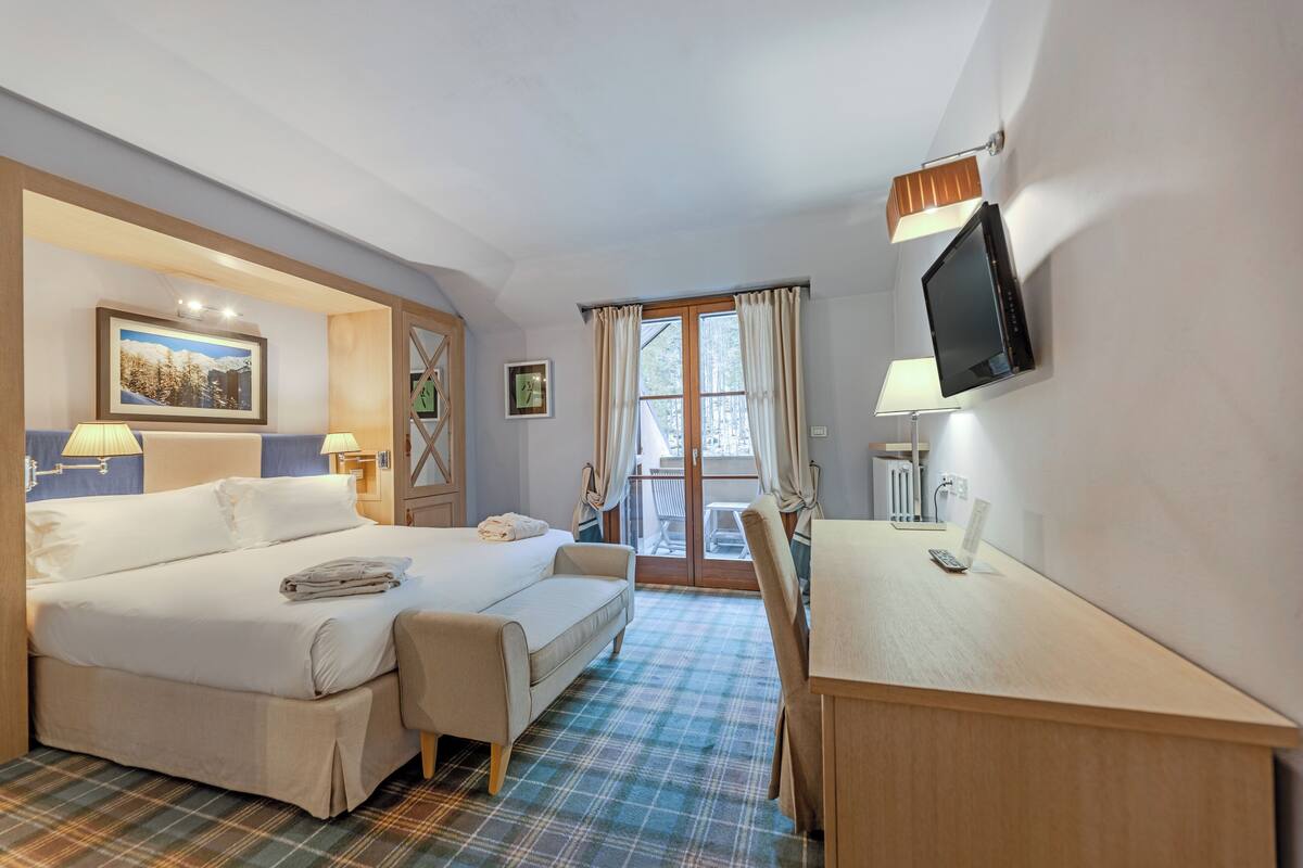 A hotel room with a bed, a desk, a chair, a television, and a window with curtains.