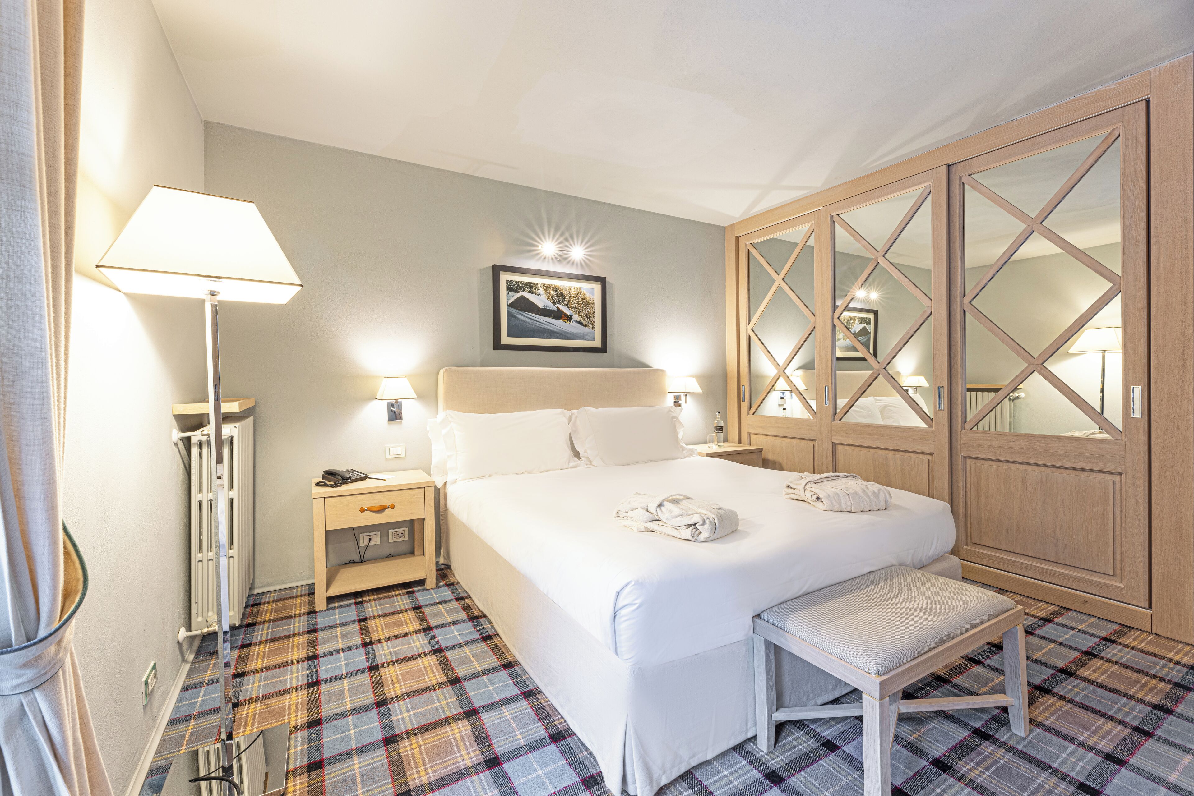 Ein Hotelzimmer mit Bett, Nachttischen, einer Bank, einem Schrank und einer Stehlampe.