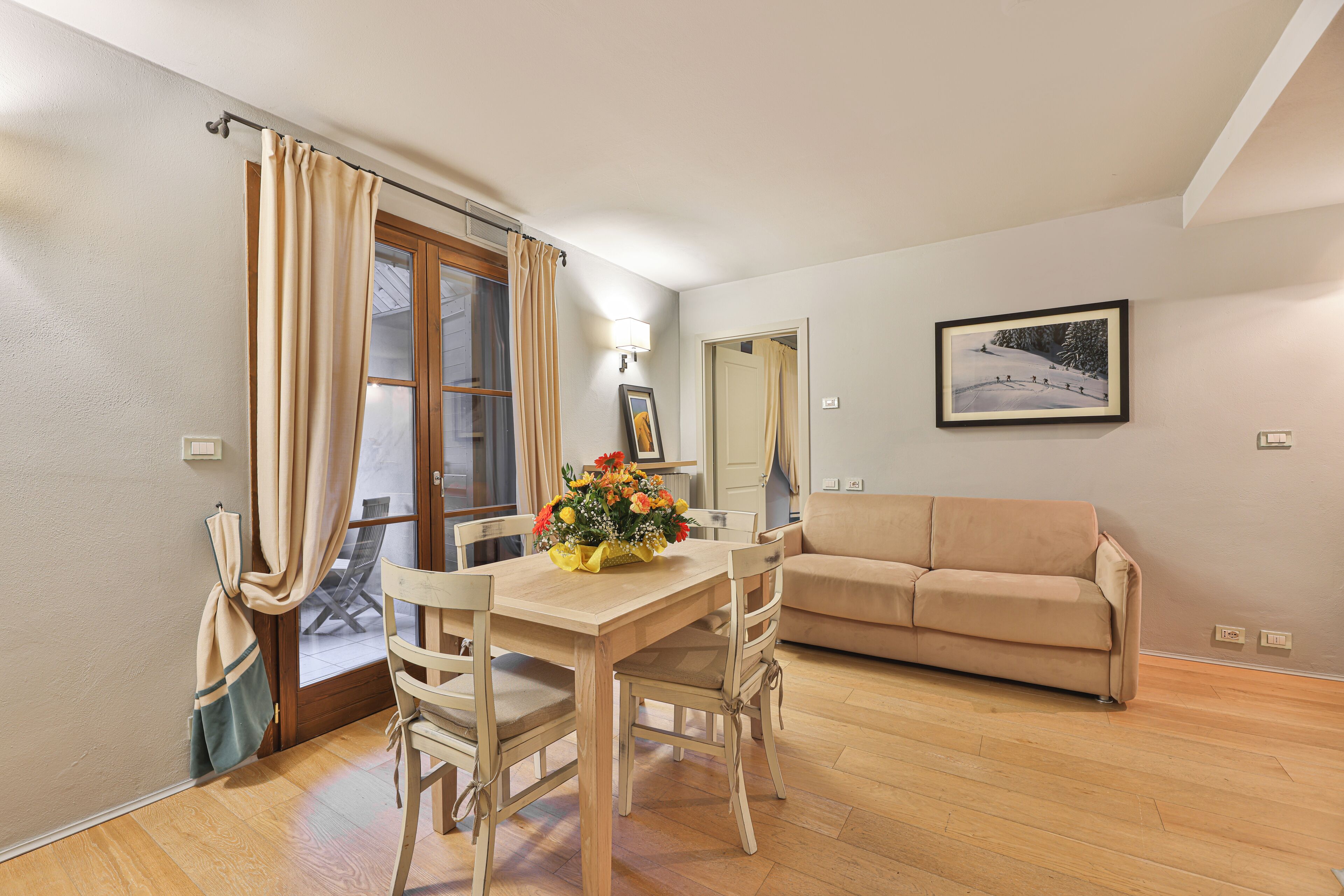 A dining area with a wooden table and chairs, a beige sofa, and a framed picture on the wall.