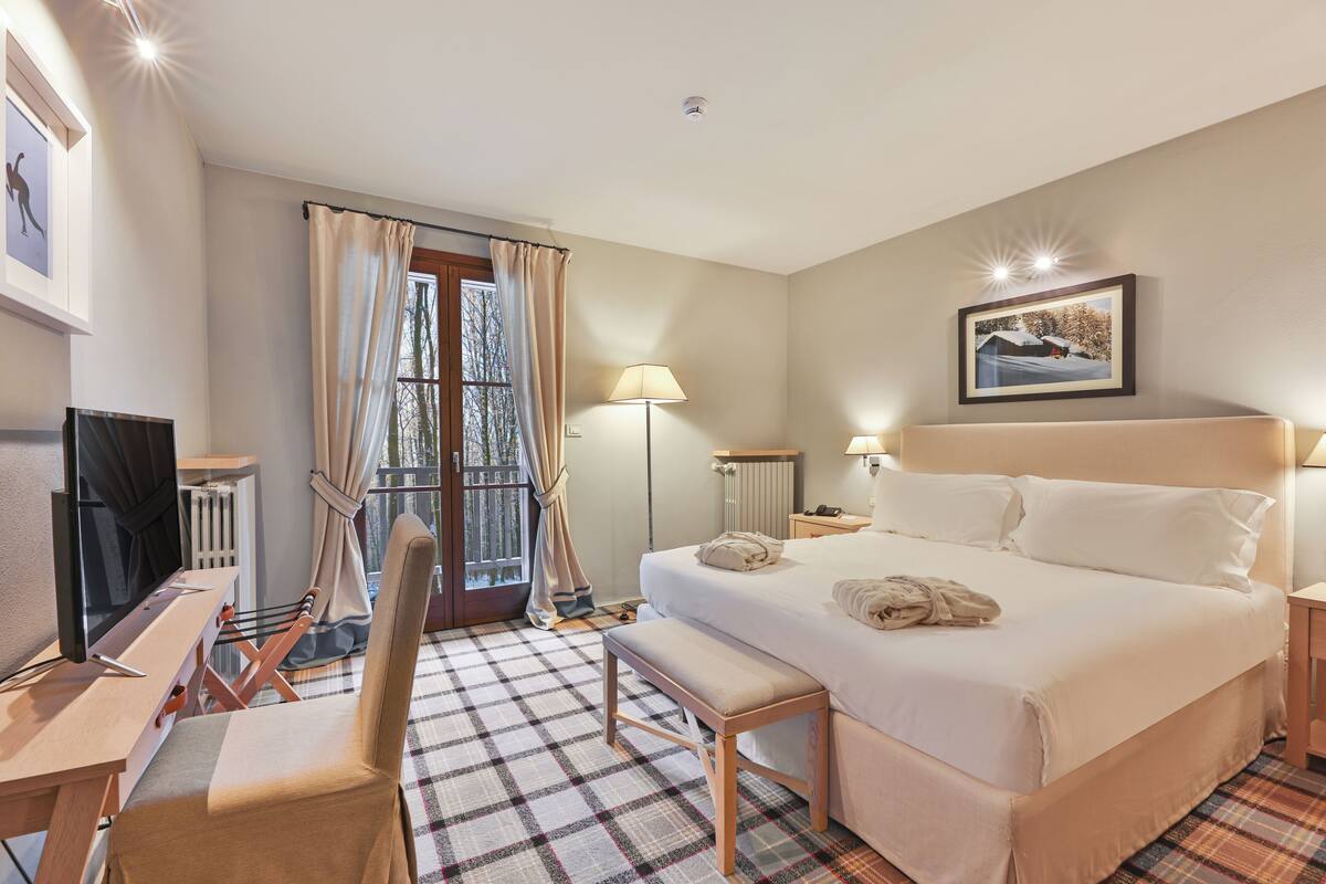A hotel room with a bed, a desk, a chair, a lamp, and a window with curtains.