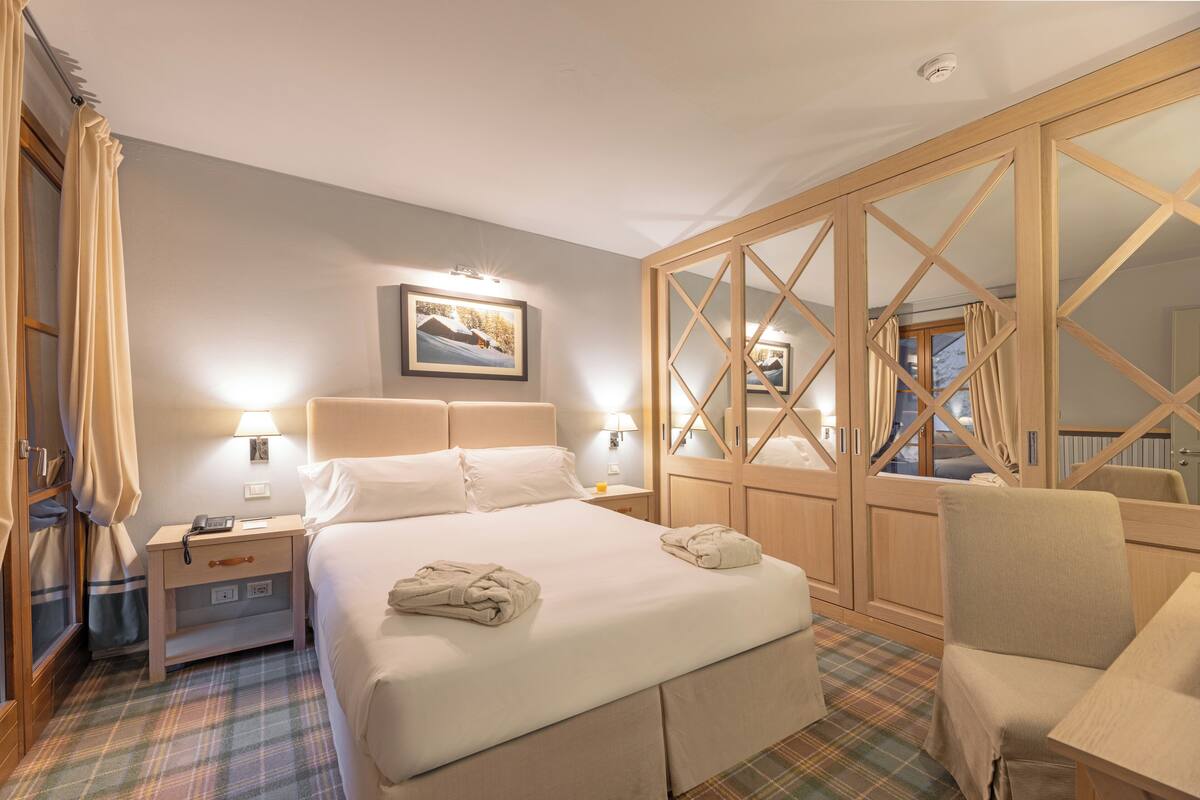 A hotel room with a bed, bedside tables, a mirror, and a wardrobe.