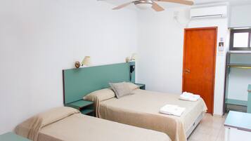 A hotel room with two beds, a ceiling fan, an air conditioning unit, a wooden door, and a small desk with a chair.