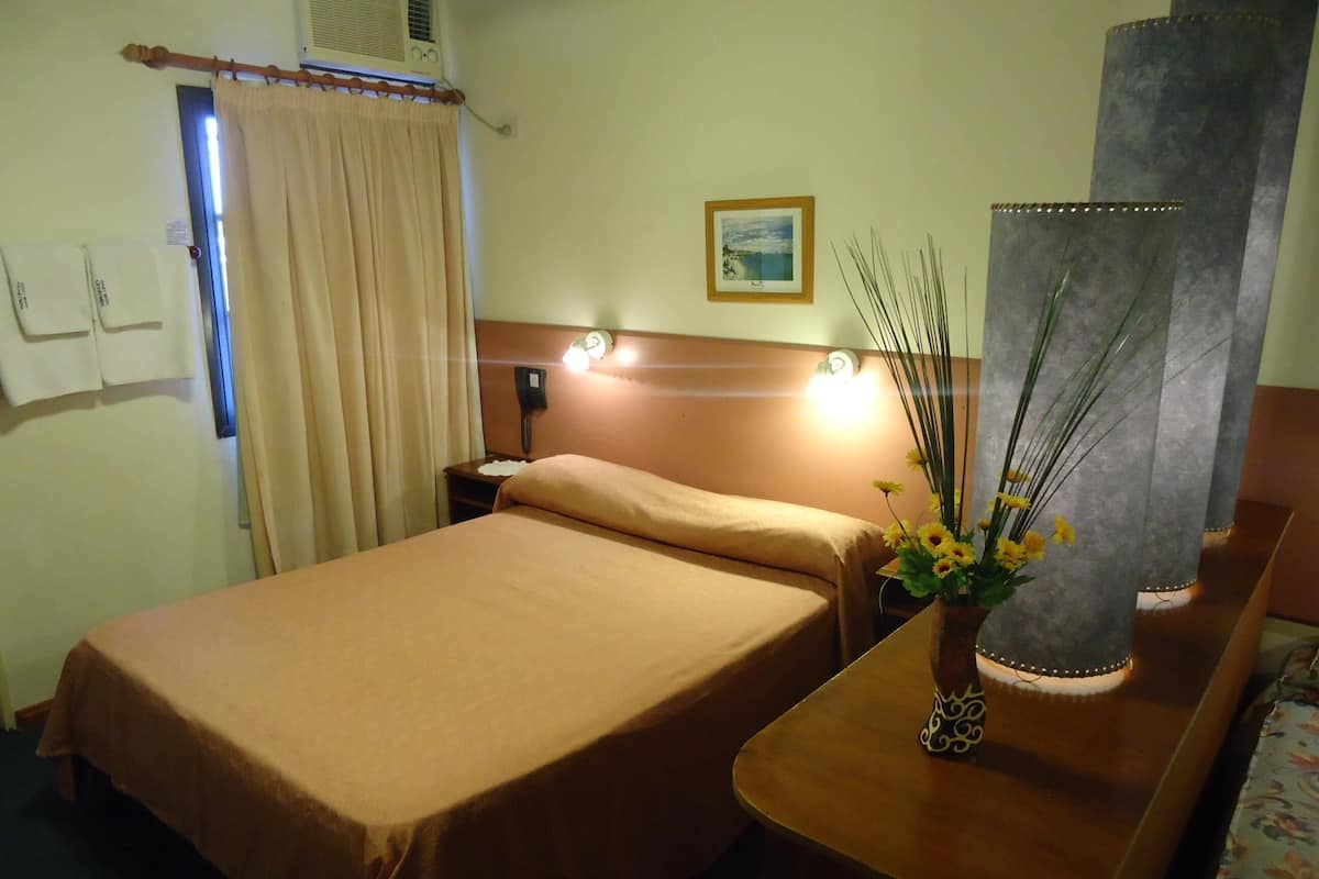 A hotel room with a bed, bedside table, lamp, and a picture on the wall.