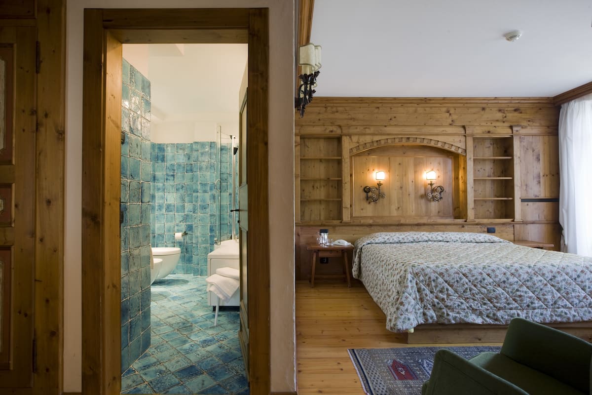 A wooden-floored bedroom with a bed, a nightstand, and a wall-mounted light fixture.