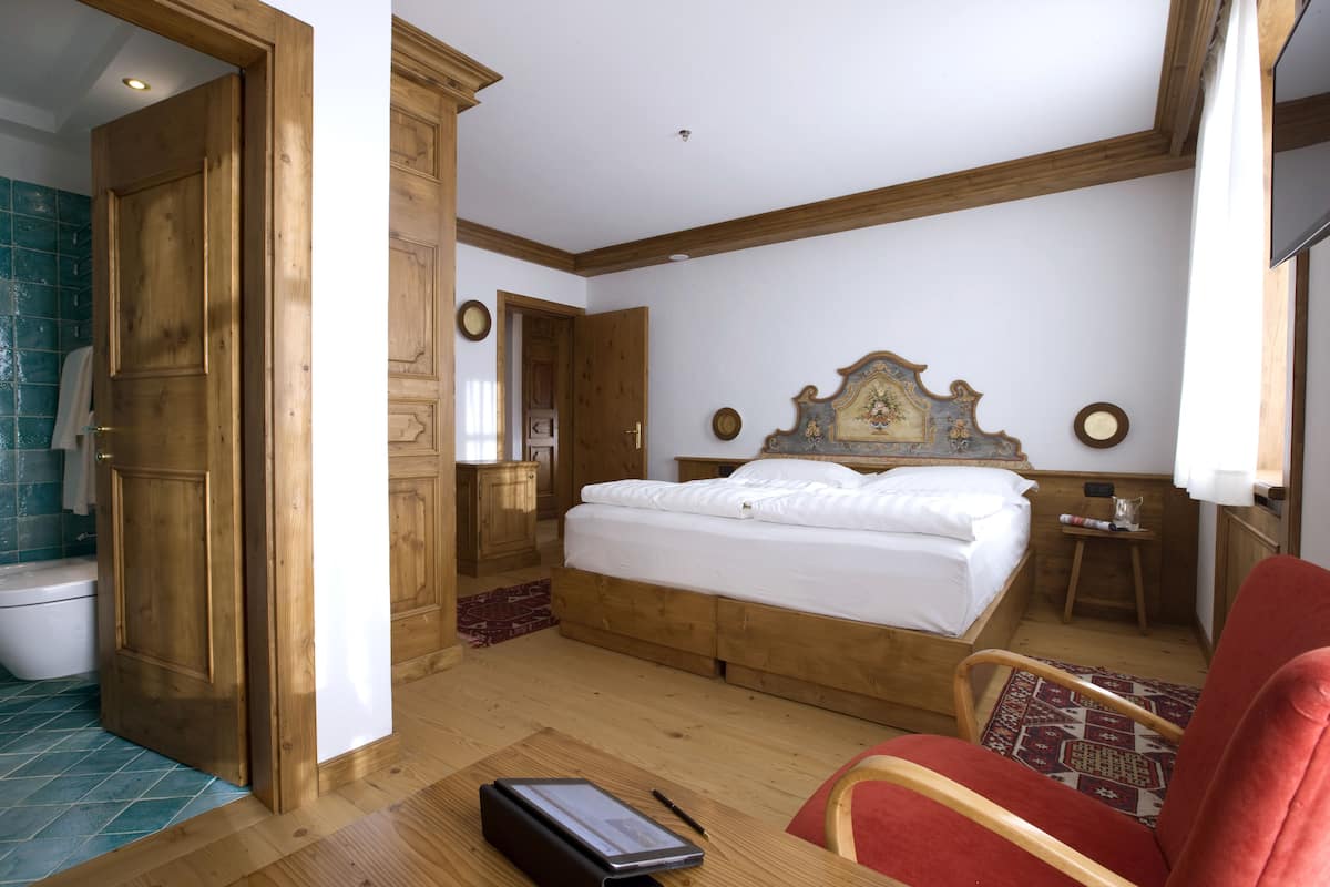 A bedroom with a wooden bed, a wooden wardrobe, a wooden door, and a red chair.