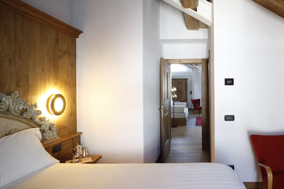 A hotel room with a wooden headboard, a bedside table with a lamp, a bed with white bedding, and a red chair.