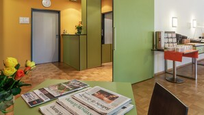 A reception area with a wooden floor, a reception desk, a clock, and a green wall. - Viavelo Hotel (Freiburg im Breisgau)
