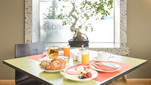 A breakfast table with croissants, eggs, and orange juice, set against a window with a bonsai tree. - Viavelo Hotel (Freiburg im Breisgau)