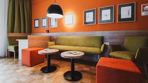 A modern waiting area with a wooden floor, orange walls, green and orange seating, and framed artwork on the wall. - Viavelo Hotel (Freiburg im Breisgau)