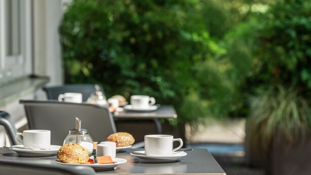 An outdoor dining area with tables set for breakfast, including cups, pastries, and a sugar container. - Viavelo Hotel (Freiburg im Breisgau)