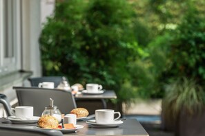 An outdoor dining area with tables set for breakfast, including cups, pastries, and a sugar container. - Viavelo Hotel (Freiburg im Breisgau)