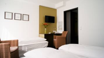 Habitación de hotel con dos camas, un escritorio con silla, televisión y cuadros en la pared.