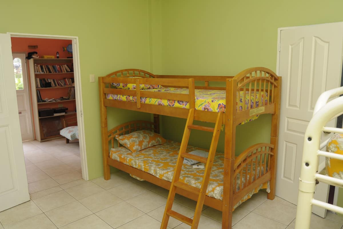 A bunk bed with a ladder, a bookshelf, and a door in a room with green walls and tiled floor.