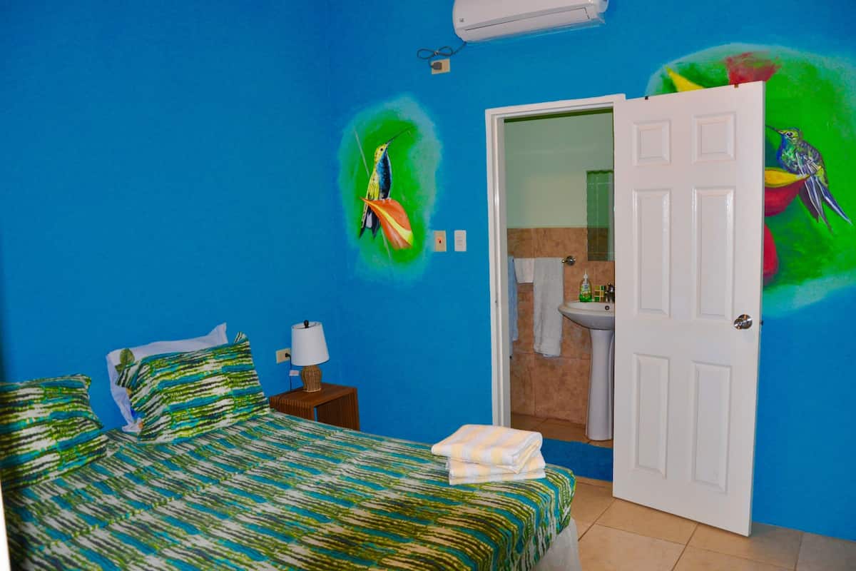 A room with a bed, a nightstand, a lamp, and a door leading to a bathroom.