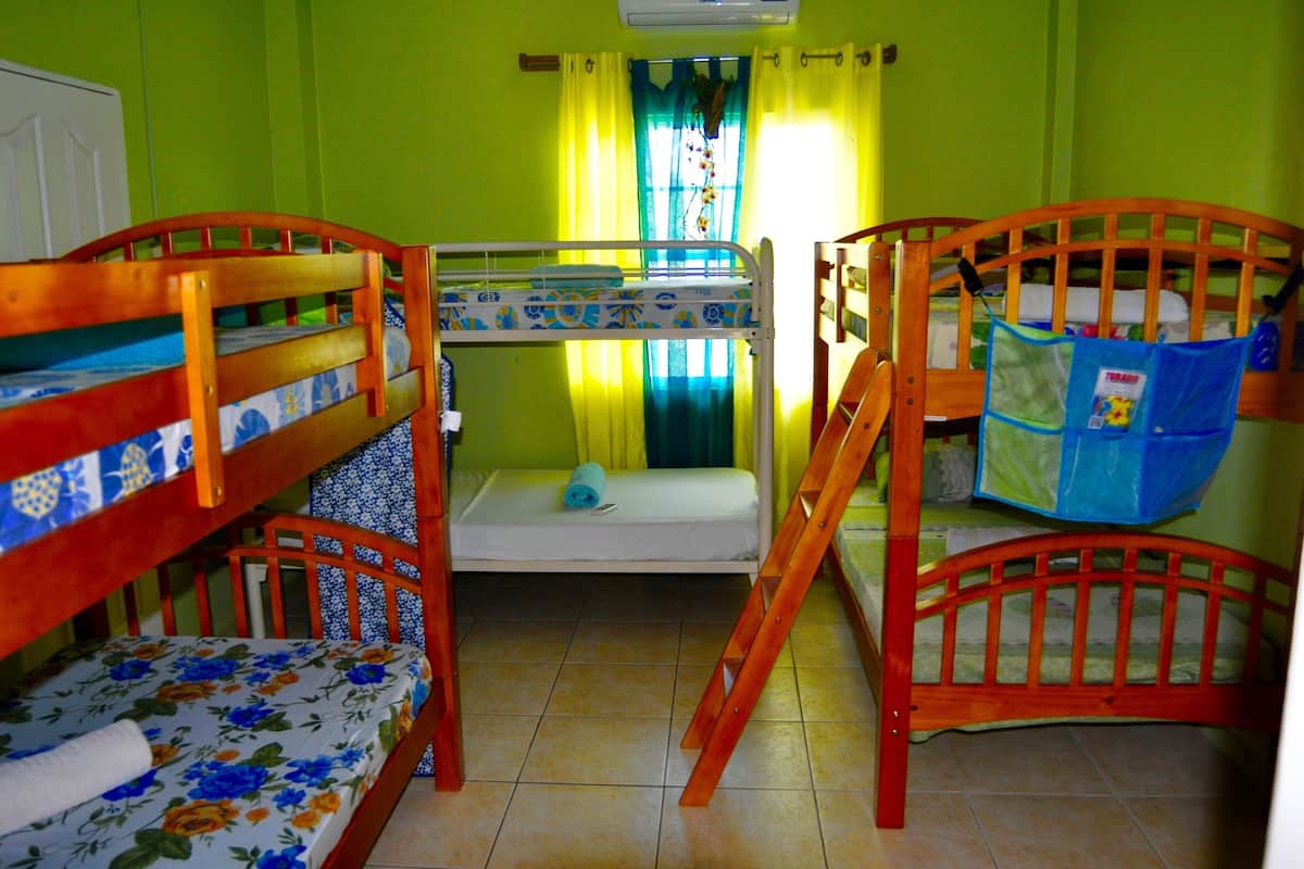 A room with two bunk beds, a window with curtains, and a small table with a blue bag.