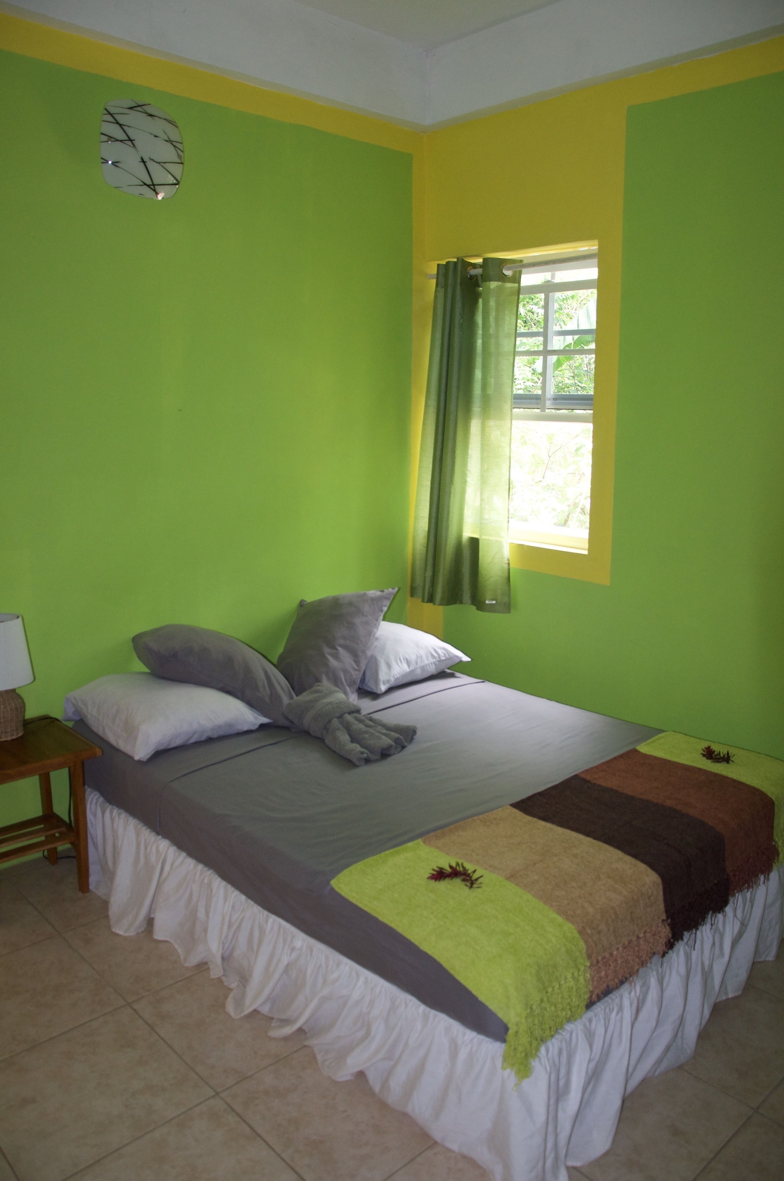 A room with a bed, a nightstand, a window with curtains, and a clock on the wall.