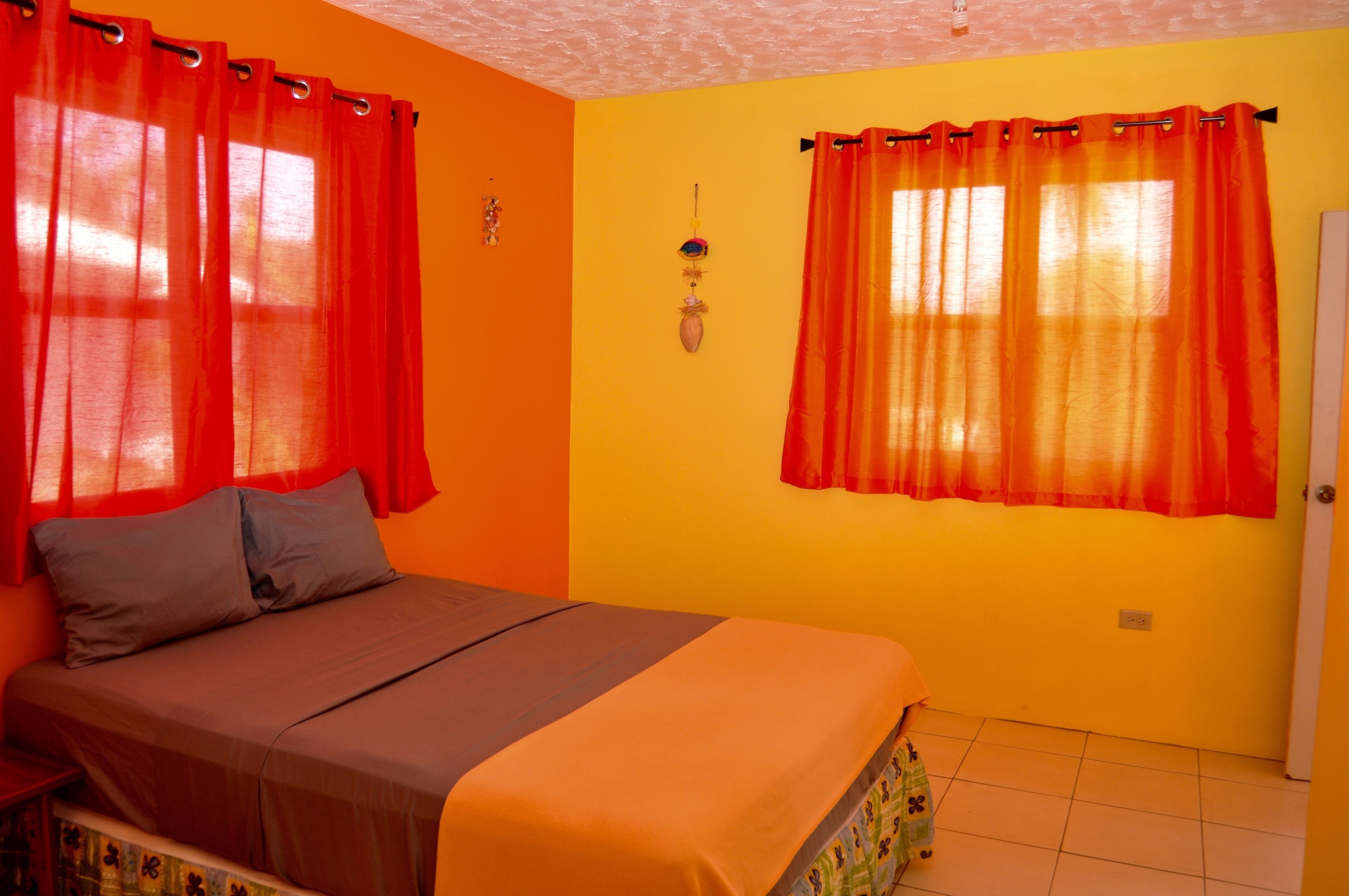 A bedroom with a bed, orange curtains, and a yellow wall.